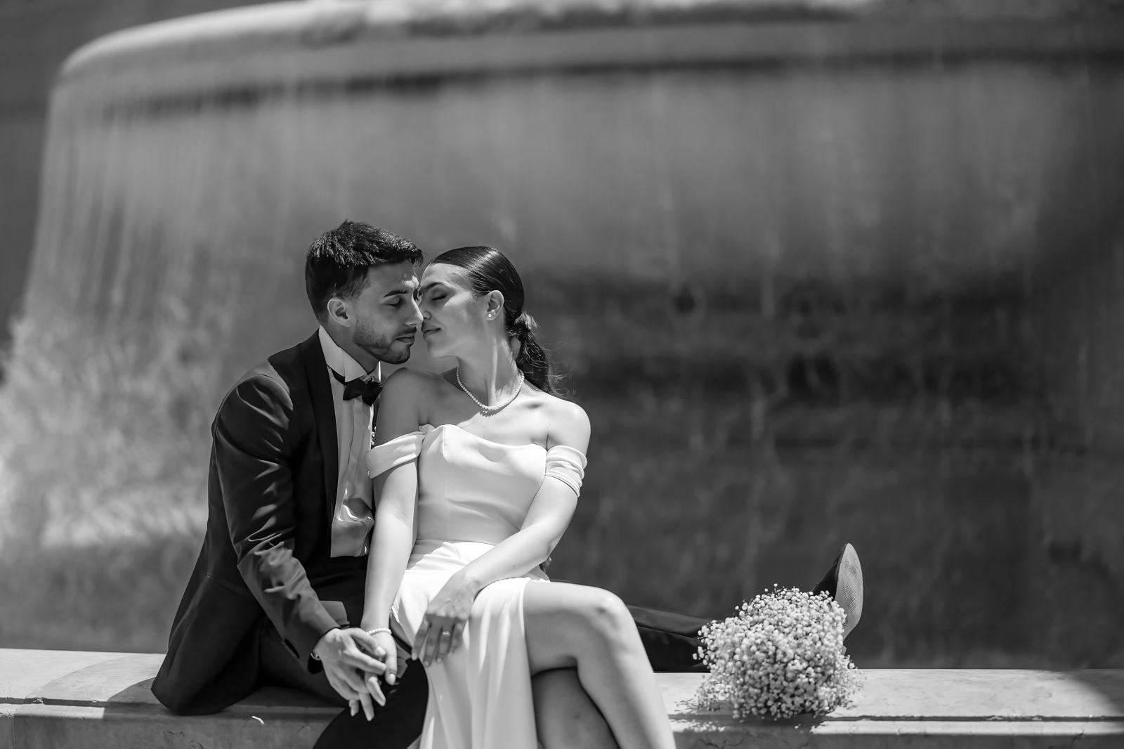 Bacio degli sposi seduti accanto a una fontana, in bianco e nero