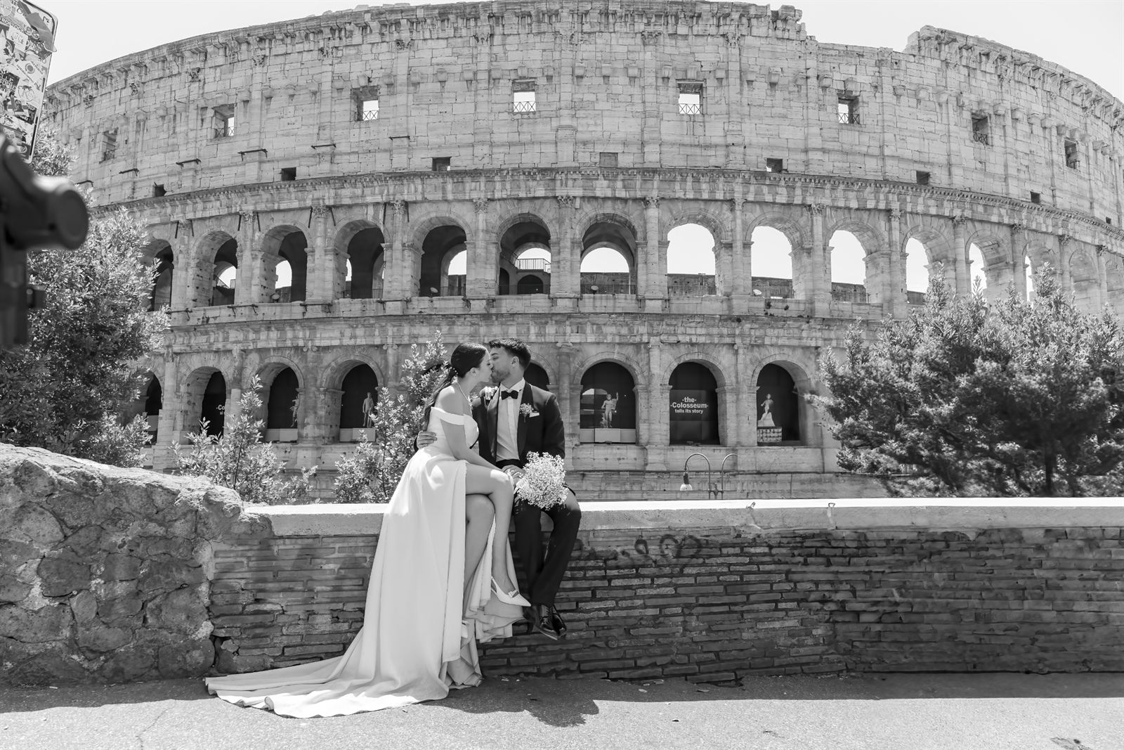 Sposi seduti su un muretto davanti al Colosseo, in bianco e nero