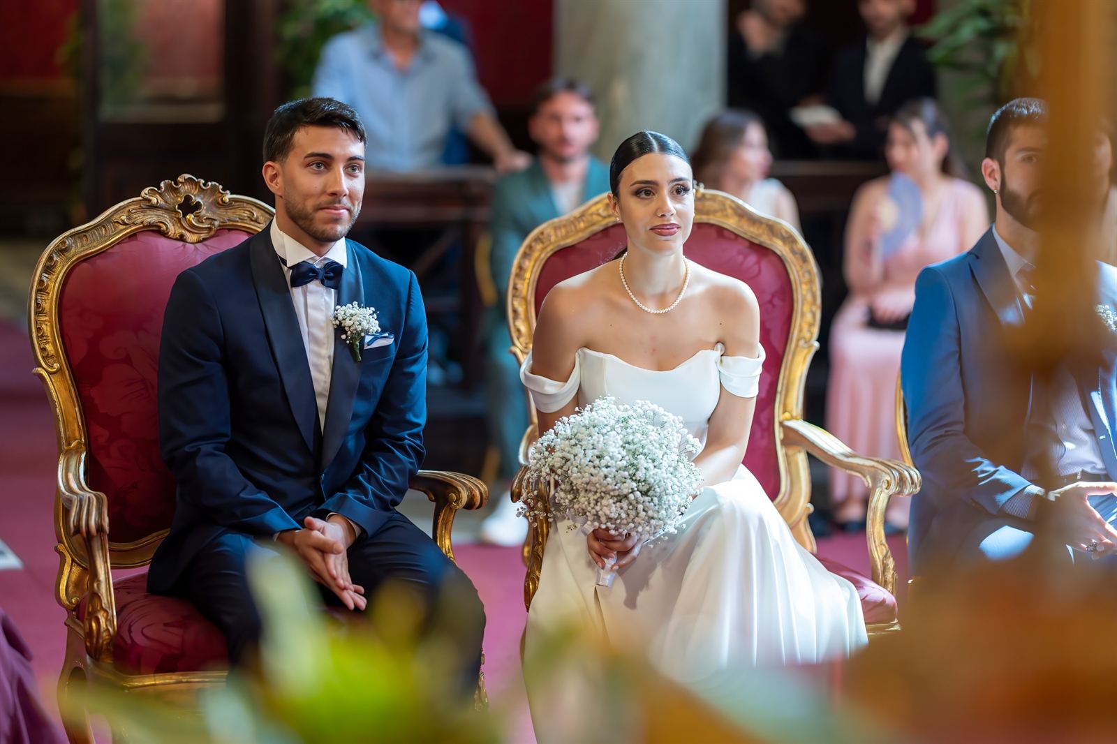 Gli sposi seduti durante la cerimonia civile, con gli invitati sullo sfondo