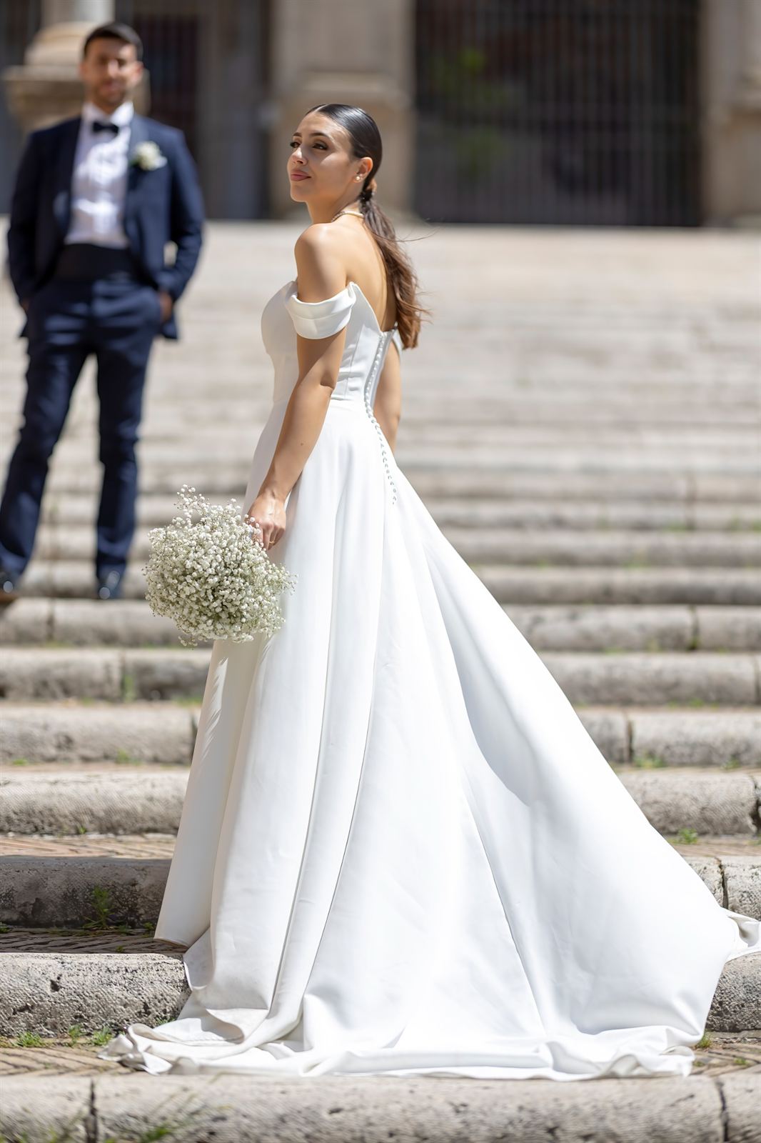 La sposa in primo piano e lo sposo sulla scalinata