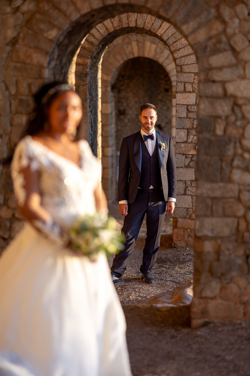 La sposa sfocata in primo piano e lo sposo sotto un arco di pietra
